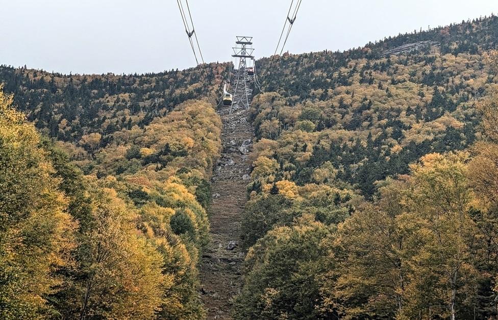 Yellow Tram car ascends Cannon Mountain with yellow and green fall foliage.